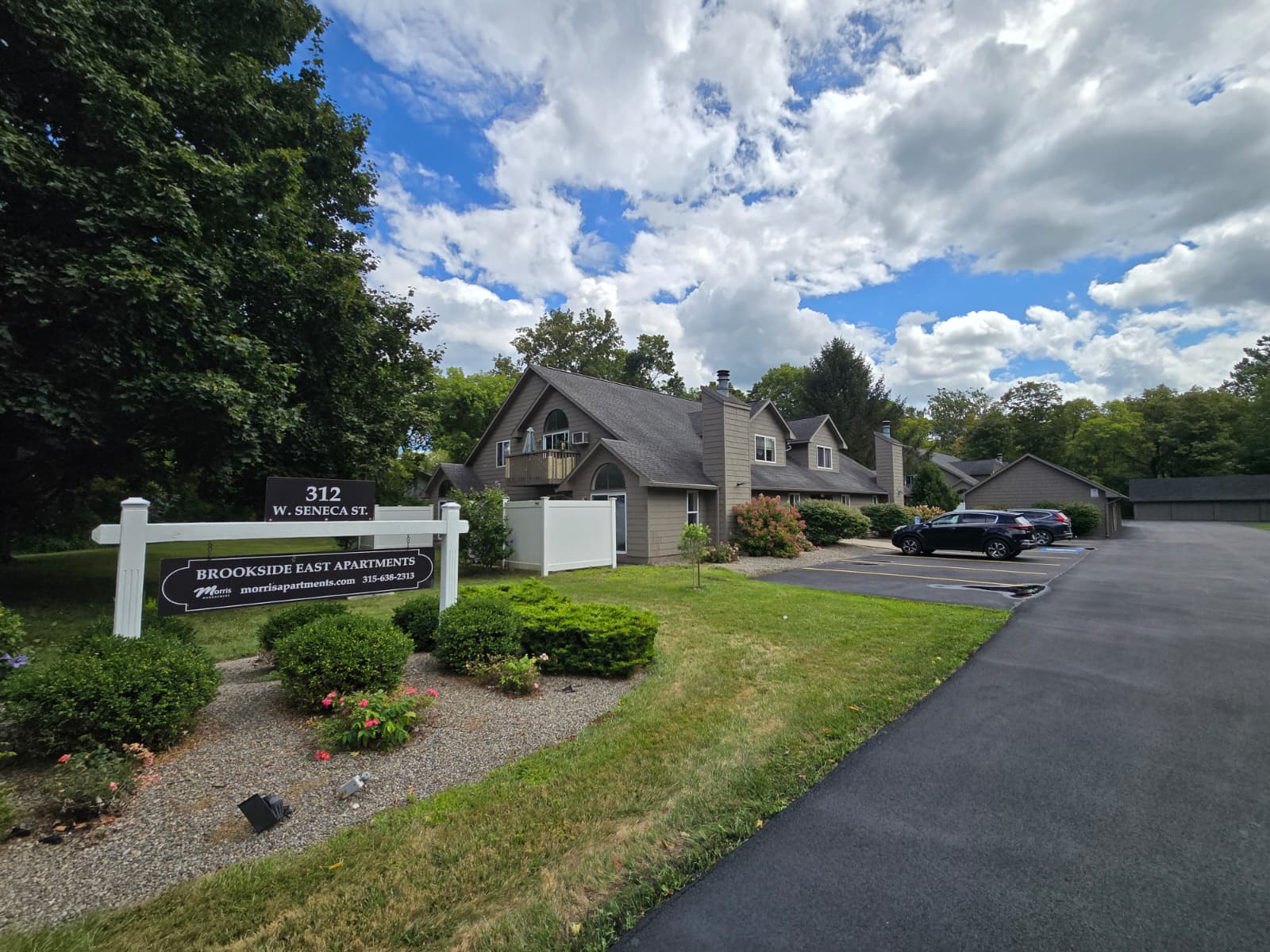 A sign for Brookside East Apartments is in front of a house.
